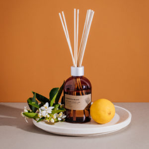 Lemongrass reef diffusers sitting on white plate with a lemon and bunch of flowers and burnt orange background