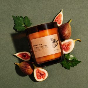 Candle labeled sweet fig resting on side surrounded by fresh cut figs